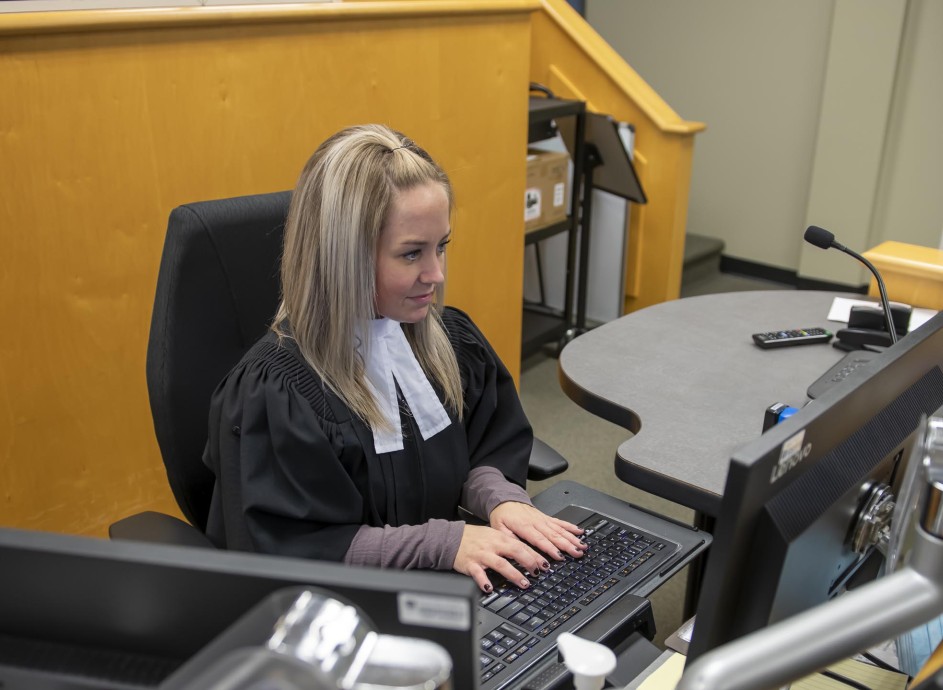 Fanshawe Court Support Services student, typing on keyboard and looking at computer monitor in courtroom setting