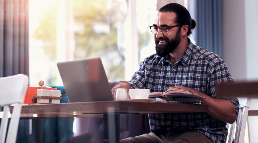 Man sitting at table, smiling at laptop with coffee cup on table