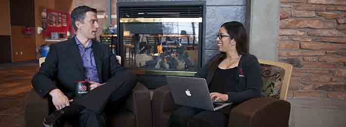 man with coffee cup sitting facing woman with laptop