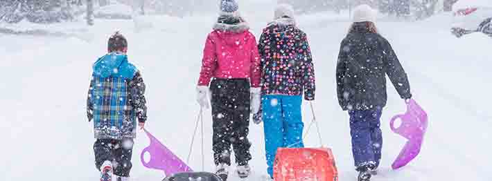 A group of kids pulling their toboggans and sleds on their way to a hill near them