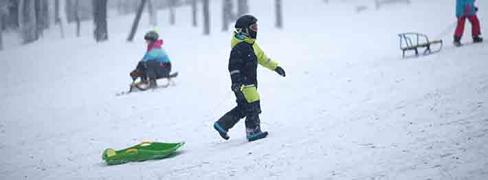 A child walking his toboggan up the hill while wearing proper head gear