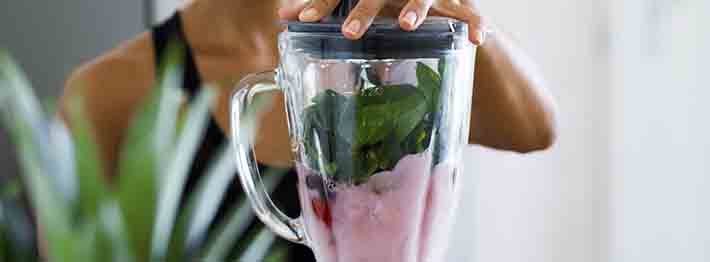 Woman blending spinach, berries, bananas and almond milk to make a healthy green smoothie