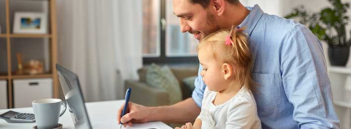 Man with child on lap working on part-time post secondary program