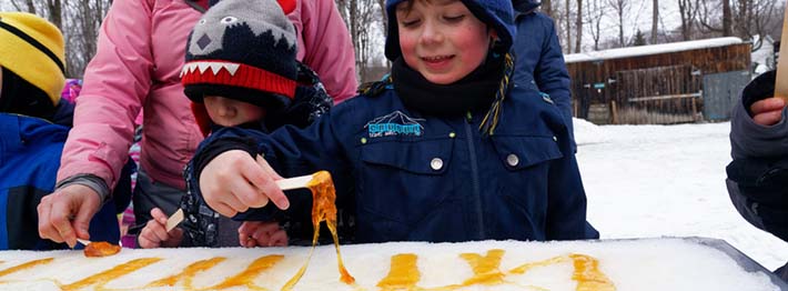 Children eating maple syrup with snow at sugar shack