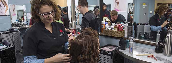 Woman styling hair in college hair stylist apprenticeship program