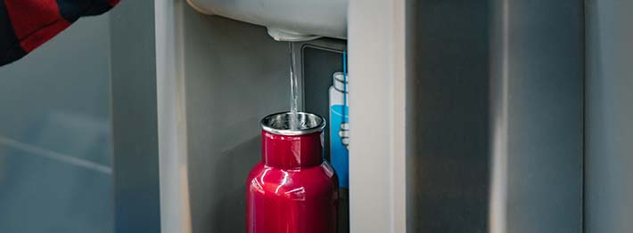 Person filling up reusable water bottle at water filling station