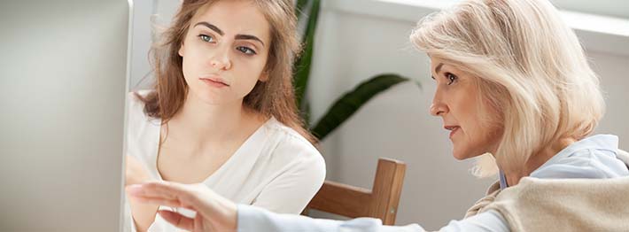 Young woman being coached at a computer by experienced professional