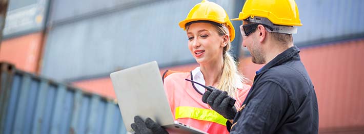 Dock workers holding a laptop in an industrial shipping yard