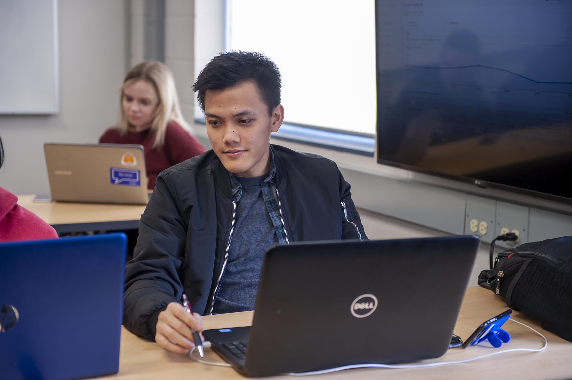 Student working on laptop in busy classroom