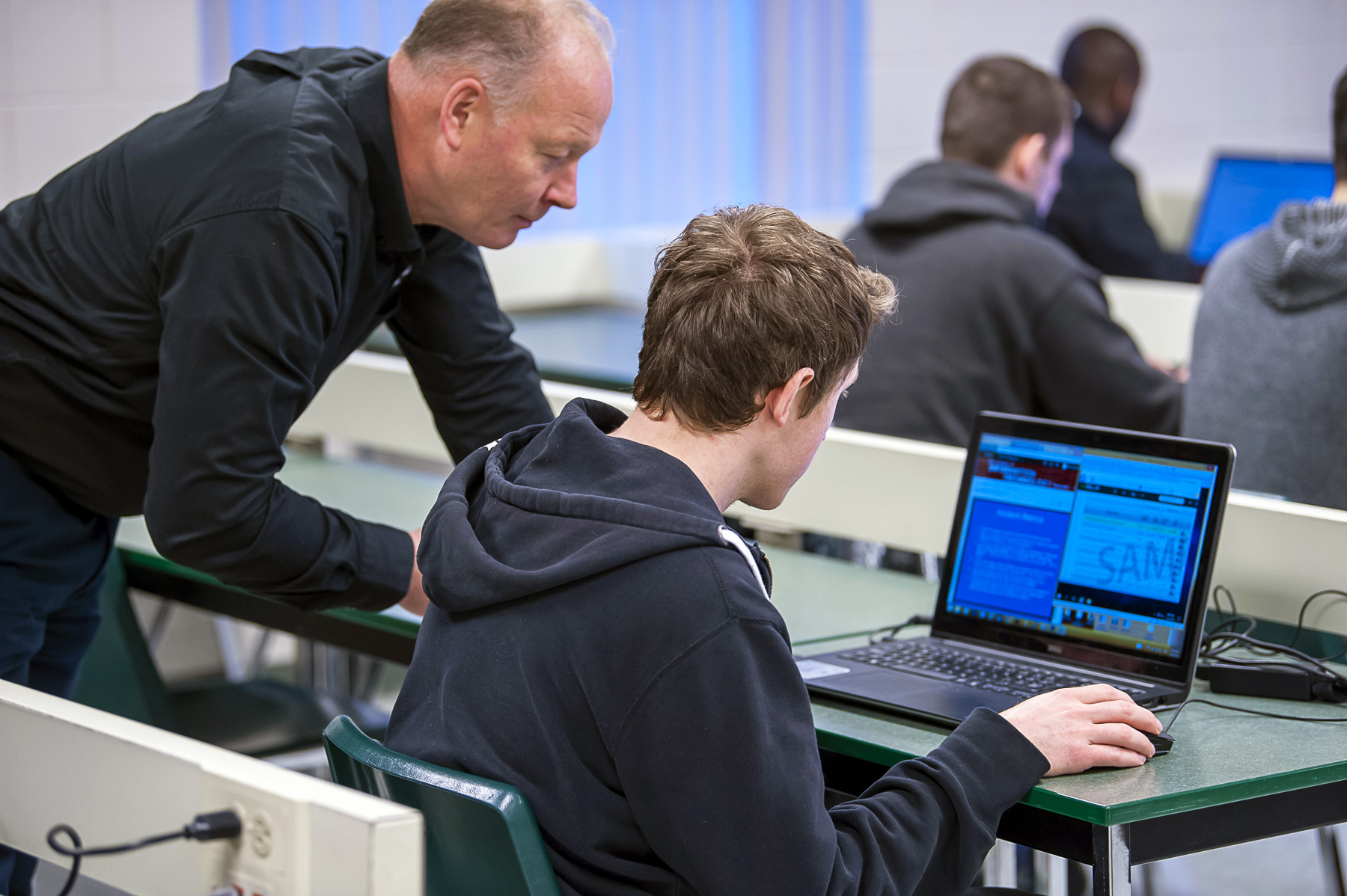 Teacher helping student with coding on computer