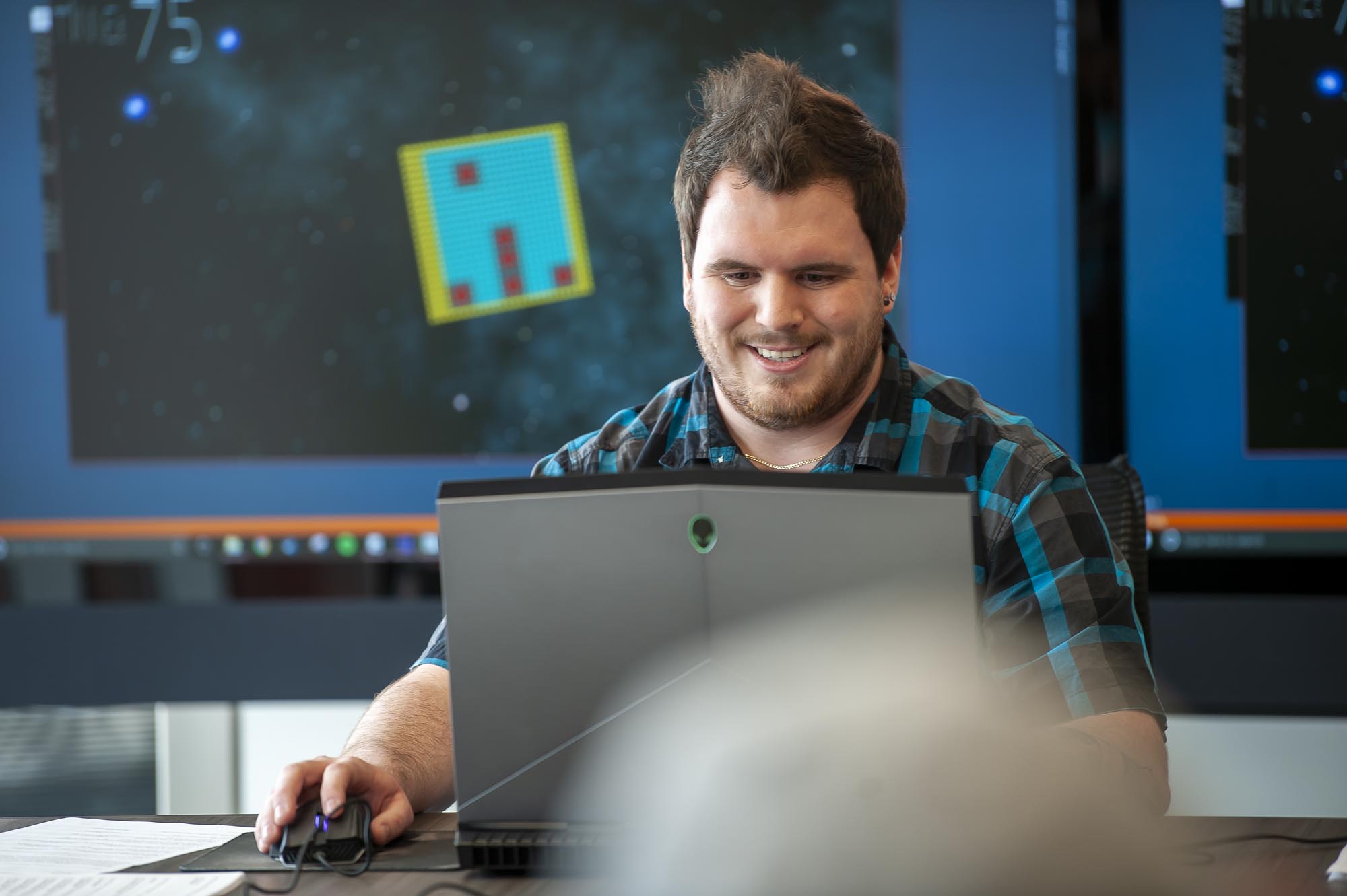 Game development student, on laptop and in front of multiple screens, presenting his work