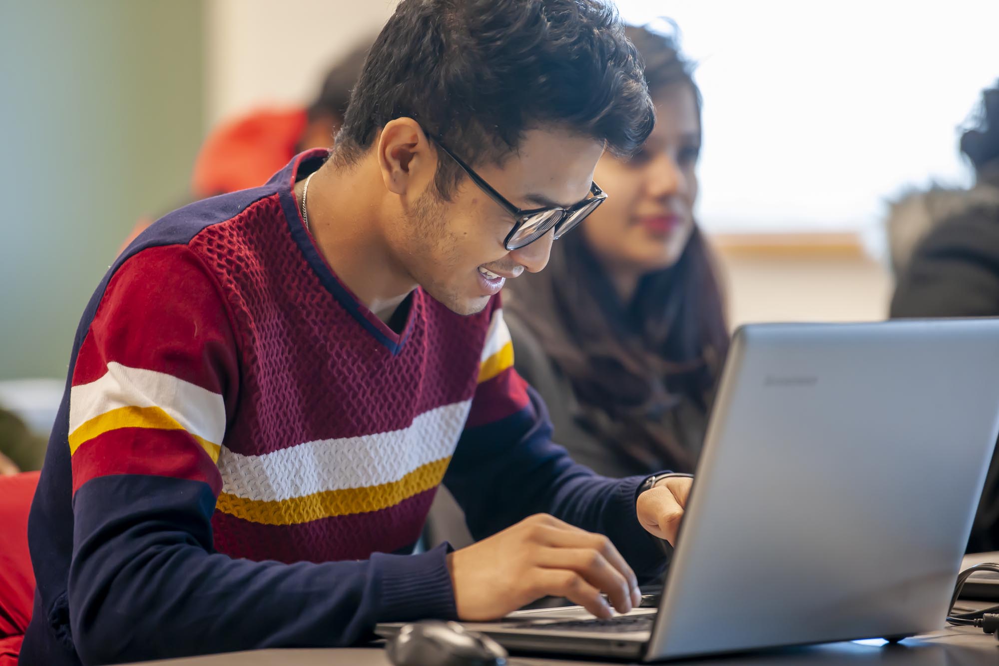 Smiling student working on laptop in busy classroom