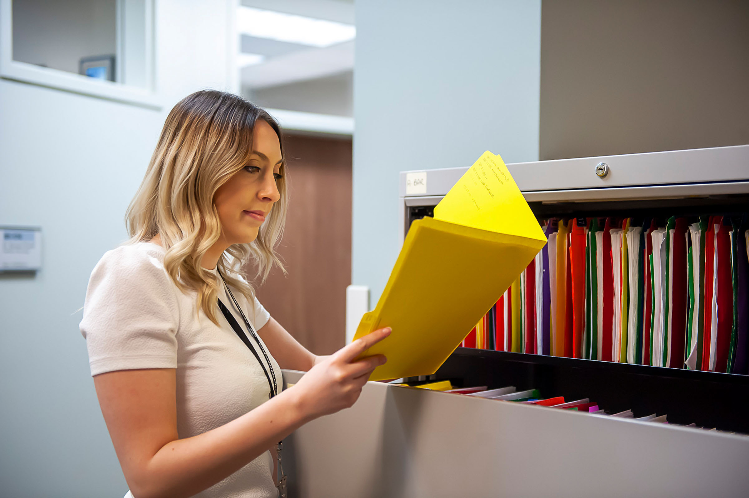 Office administrator looking at a yellow folder in a filing cabinet