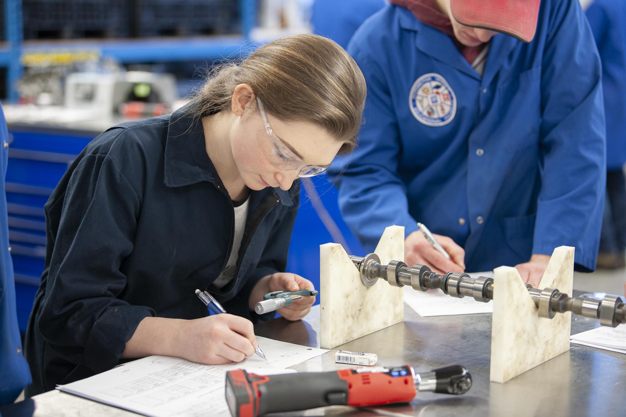 Automotive Service Technician student writing at a table in an automotive lab
