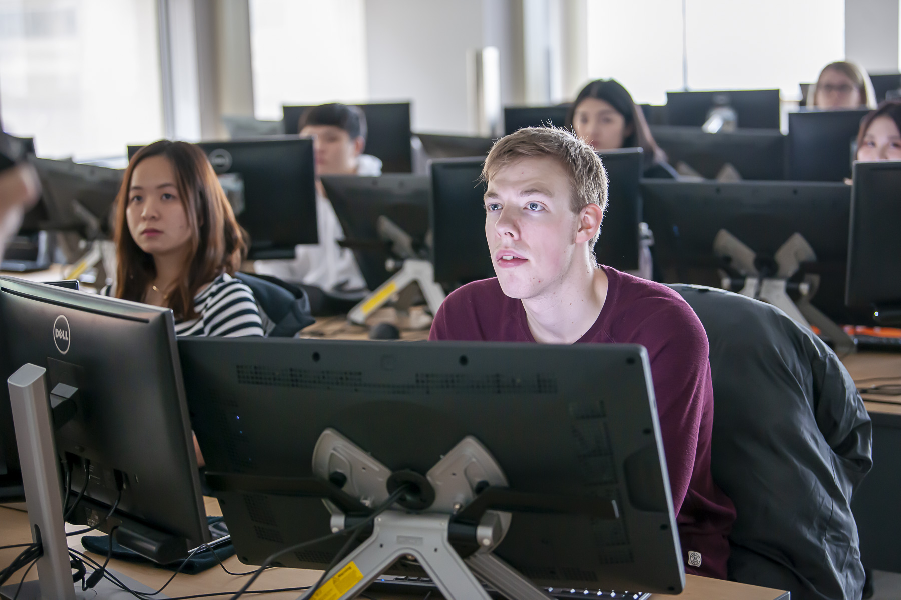 Student in busy computer lab listening to professor
