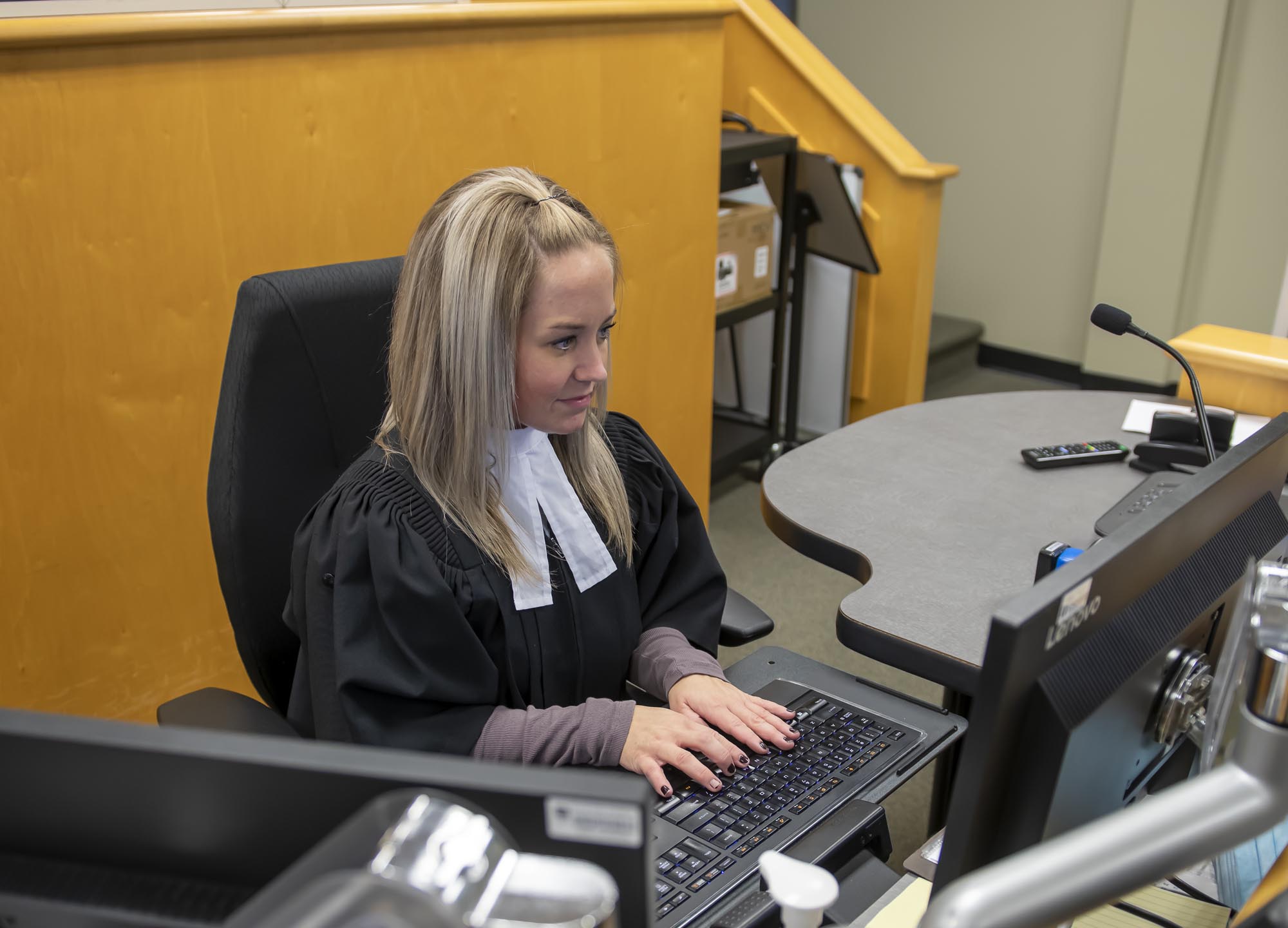 Fanshawe Court Support Services student, typing on keyboard and looking at computer monitor in courtroom setting