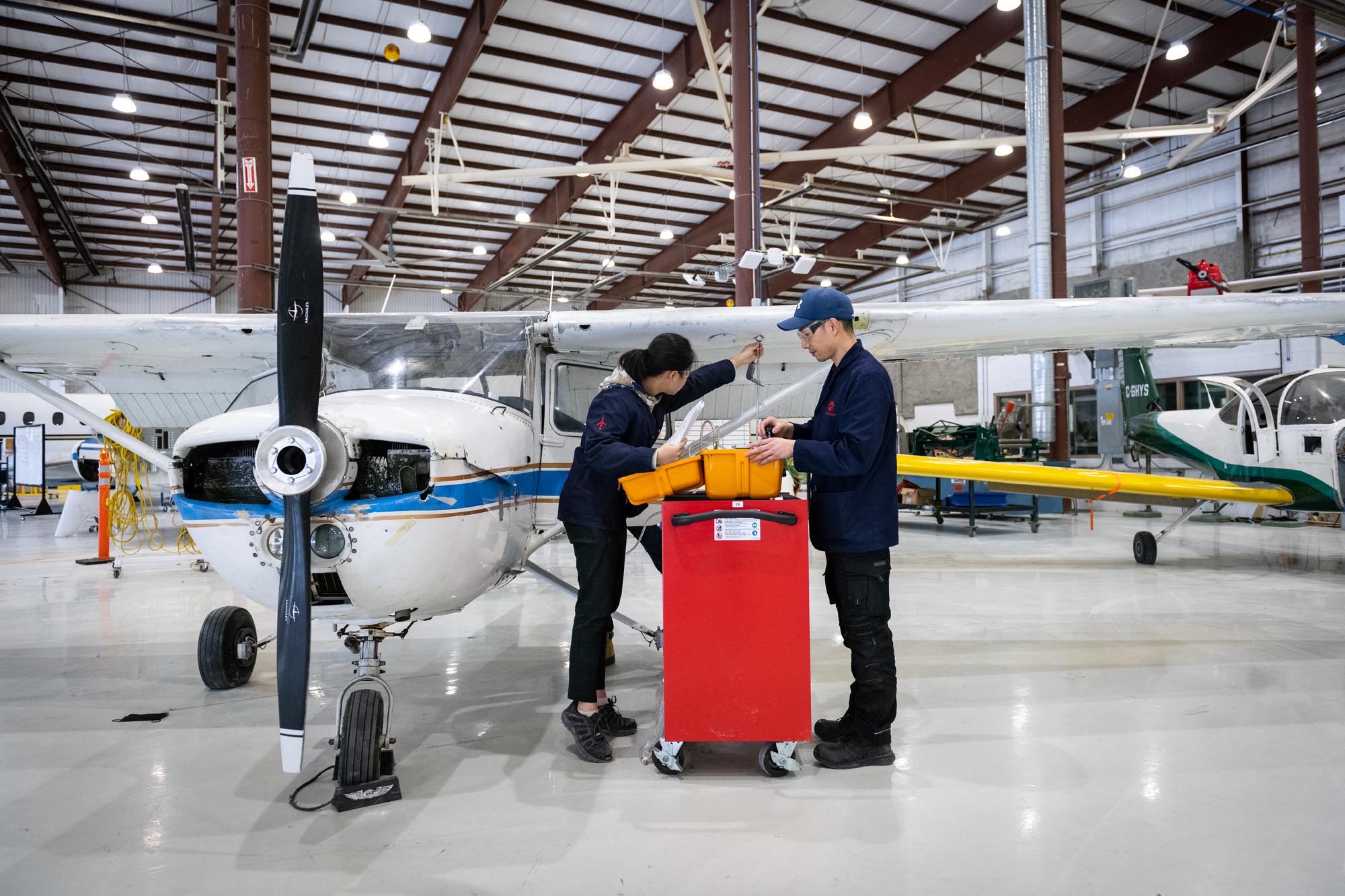 Two Aviation Technician Avionics Maintenance students working in front of airplane in Jazz Hangar at Fanshawe College