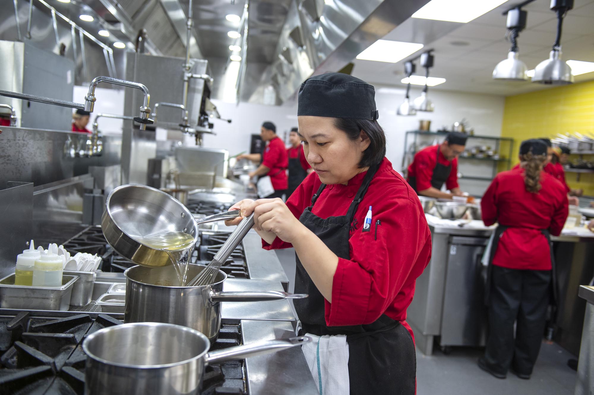 Culinary student pouring liquid into pot on stove in culinary lab