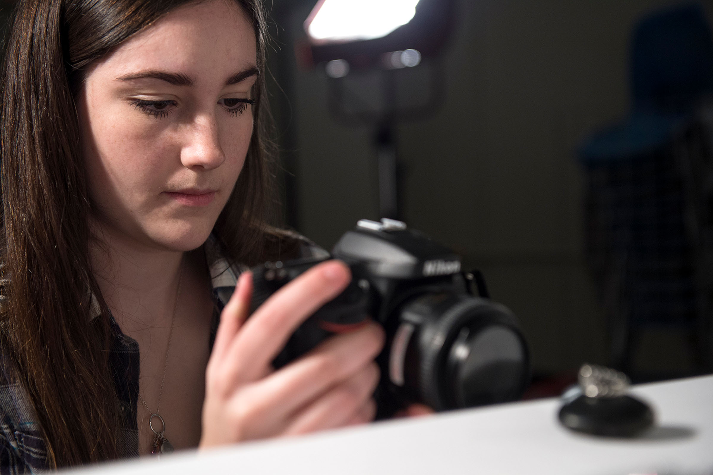 Girl with camera taking photo of small object in studio