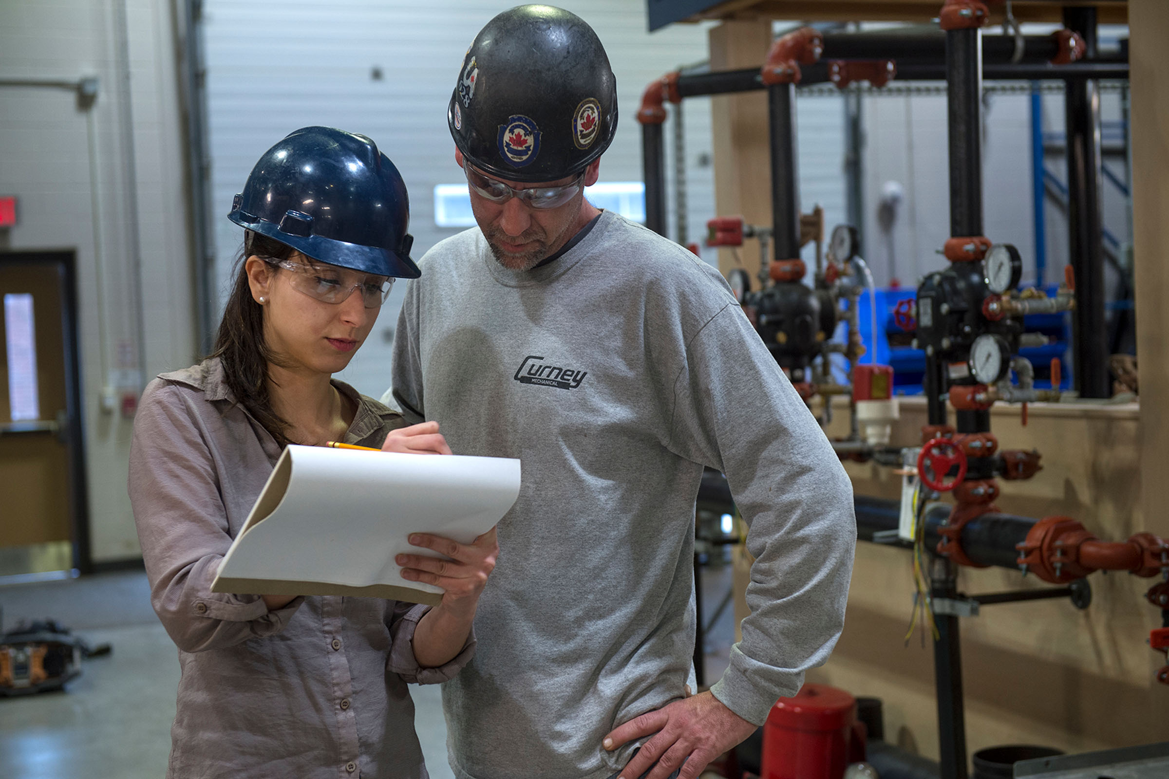 Two project managers with hard hats looking at plans on clipboard