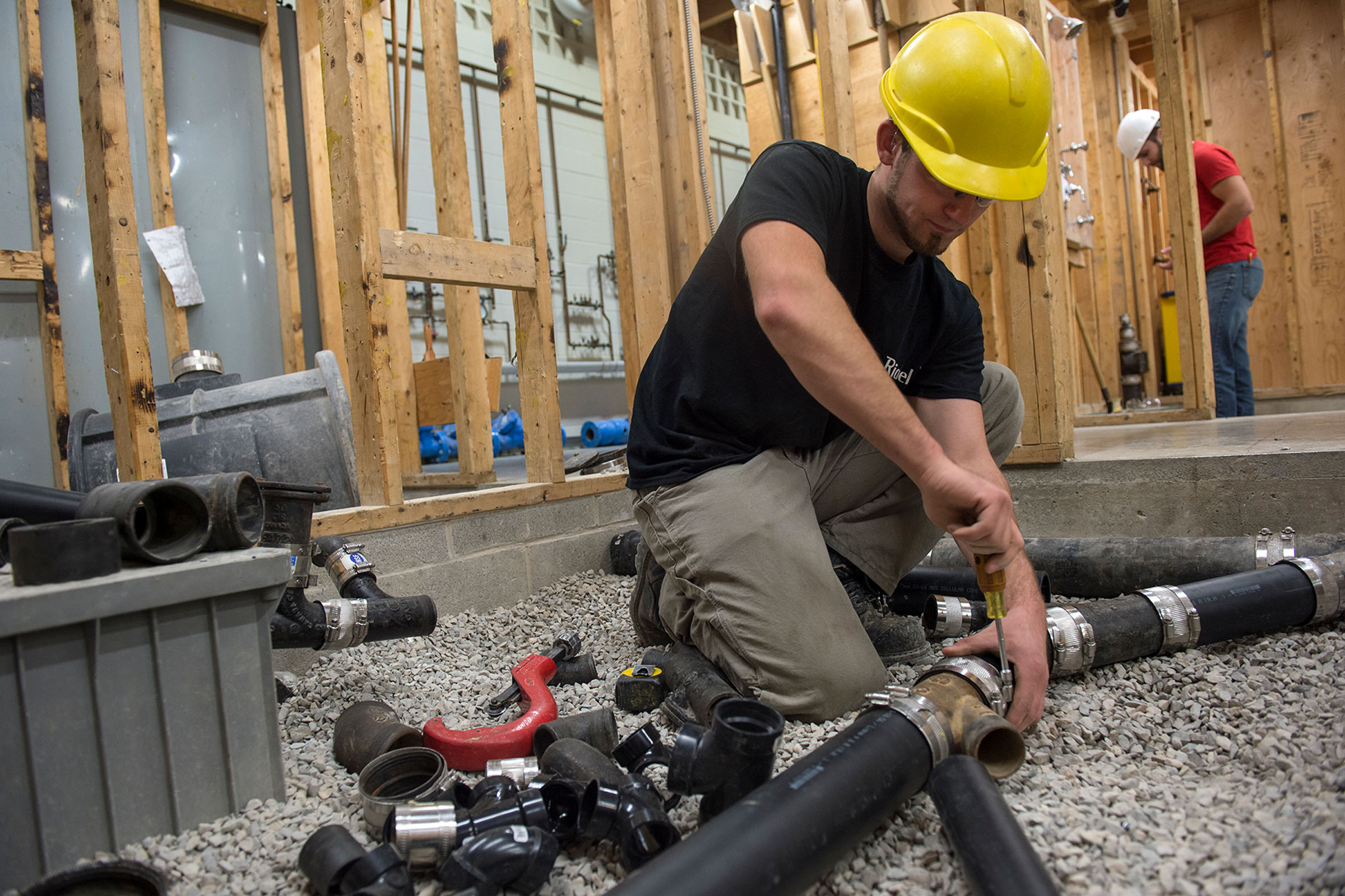 Plumbing student tightening pipes in construction setting