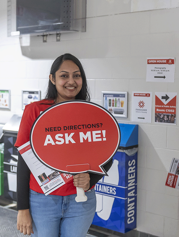 woman standing with sign that says Ask Me