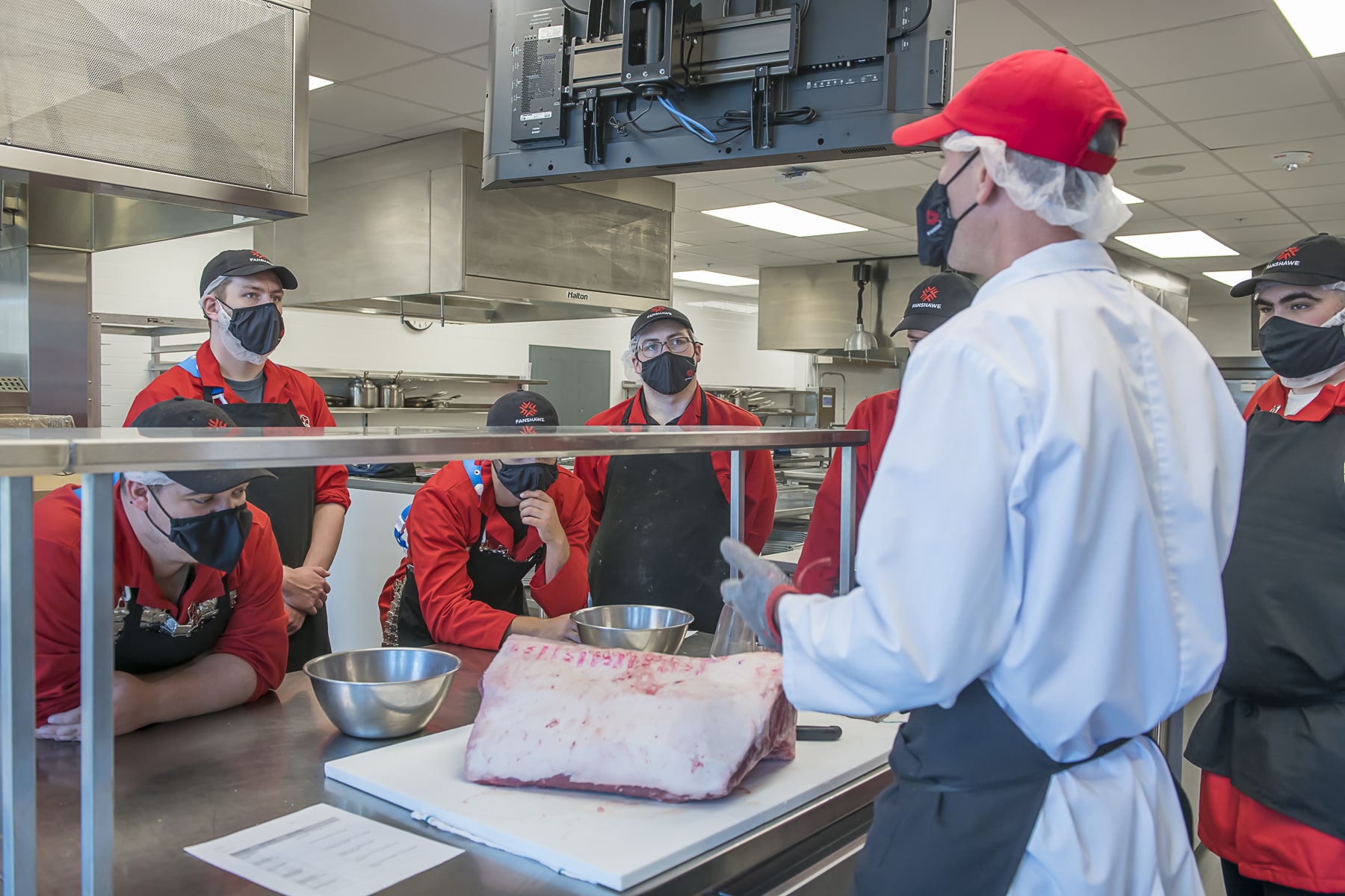 man stands in front of butcher counter talking to butchery students