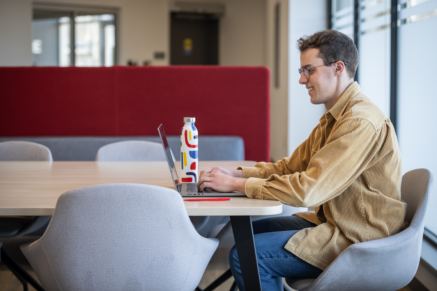 Smiling student working on laptop in common area at Fanshawe College