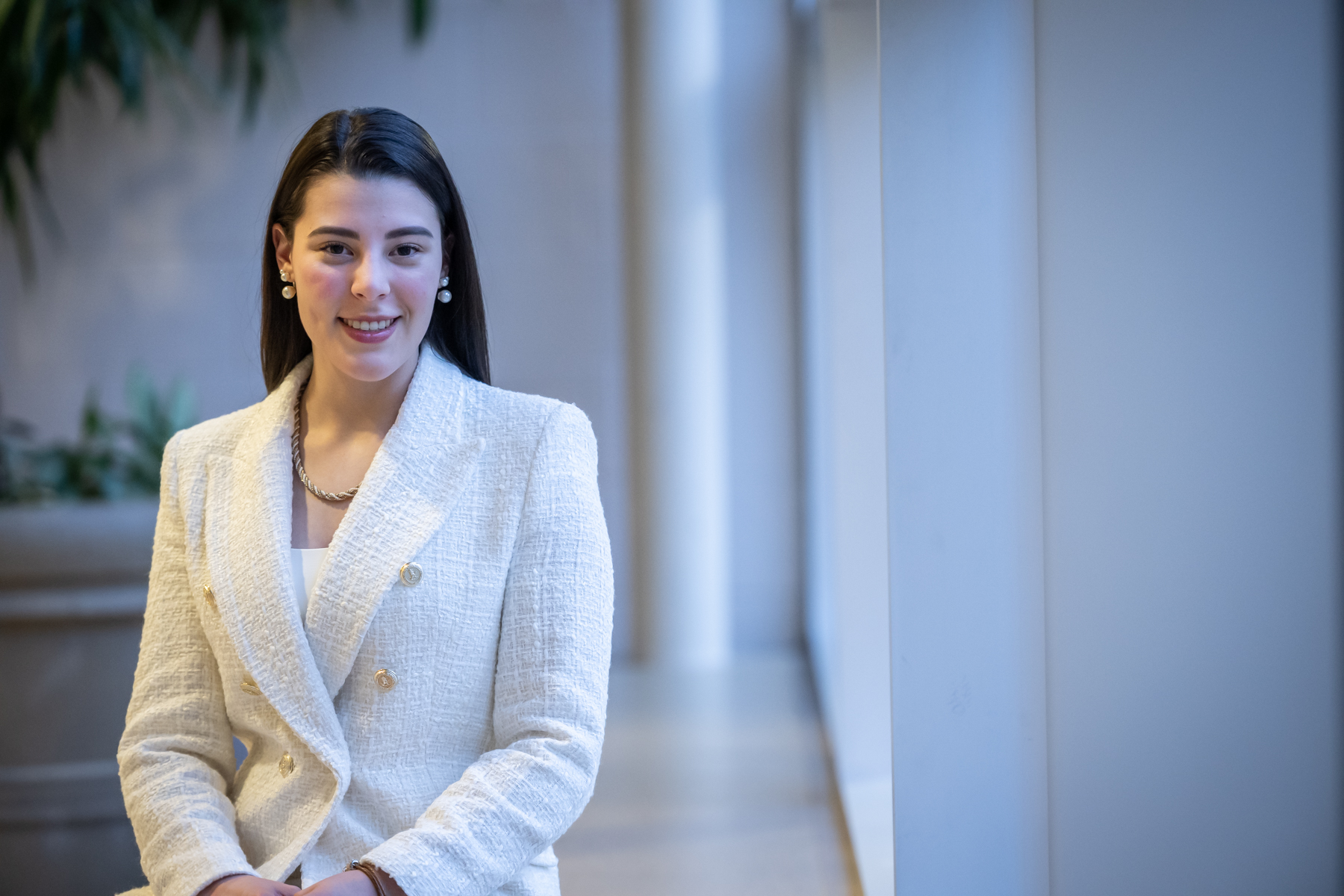 A female accounting student smiling and posing while sitting on a bench in a bright hallway at the Fanshawe College campus