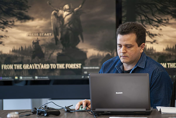man sits in front of large screens showing video game while working on a computer