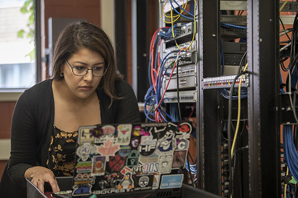 woman sits in front of server looking at a laptop screen