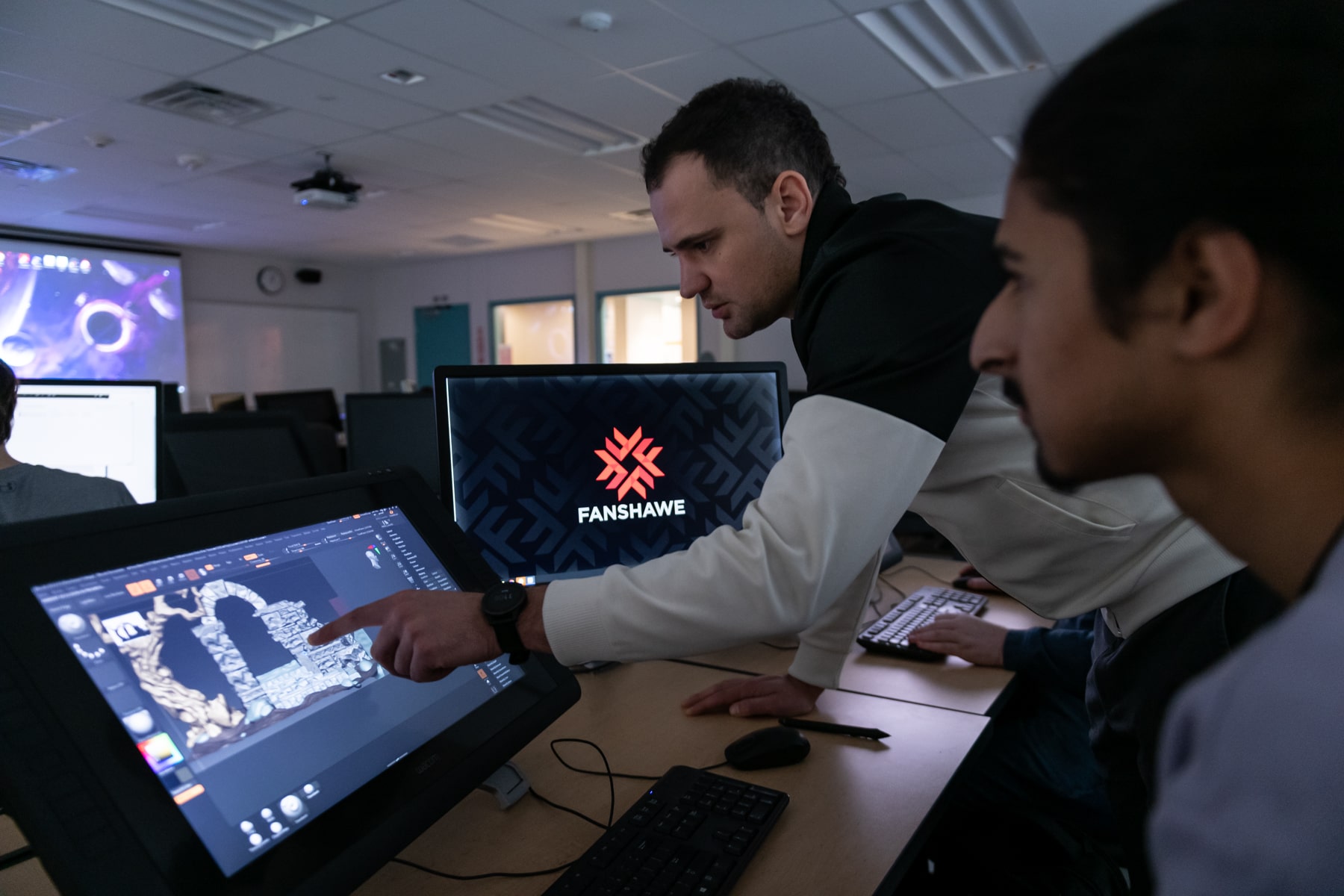 man points at video game concept on screen while student looks on