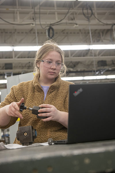 woman works with tools while looking at a laptop