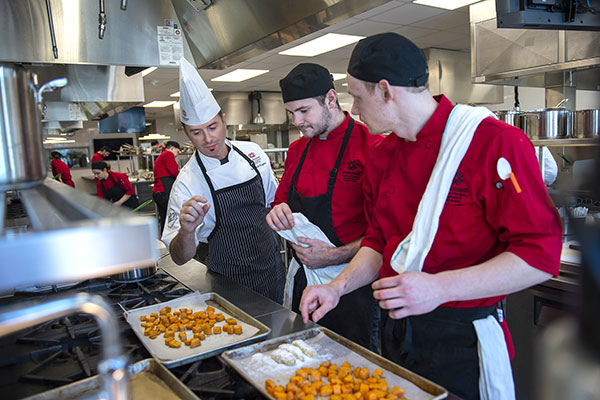 two students listen to a chef while standing over baking sheets