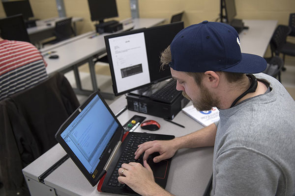 person sits in classroom, coding on laptop