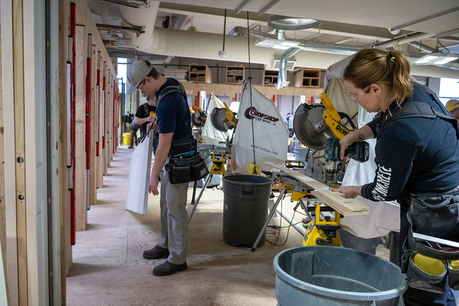 one person drills while another holds drywall in a workshop