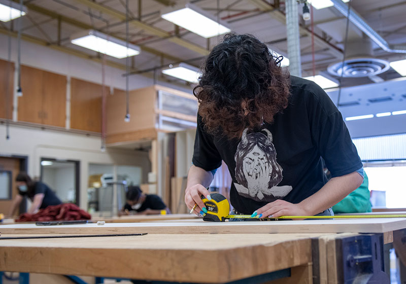 Student using a tape measurer to measure a piece of wood