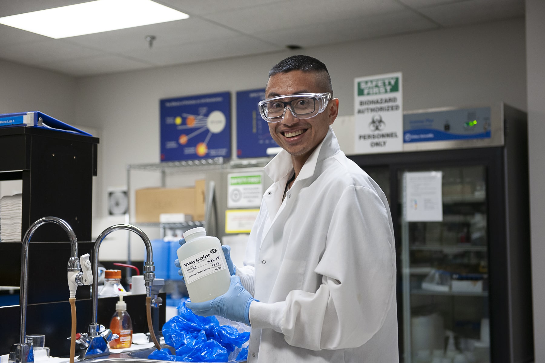 Celebrate our Alumni alum smiles while holding a bottle in a lab