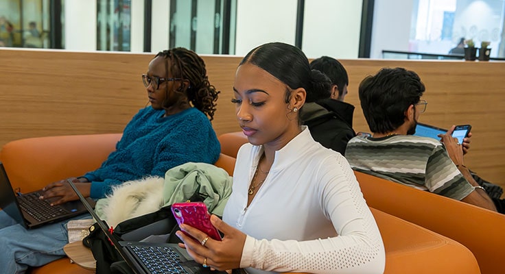 Student sits in study space with other students while looking at their phone