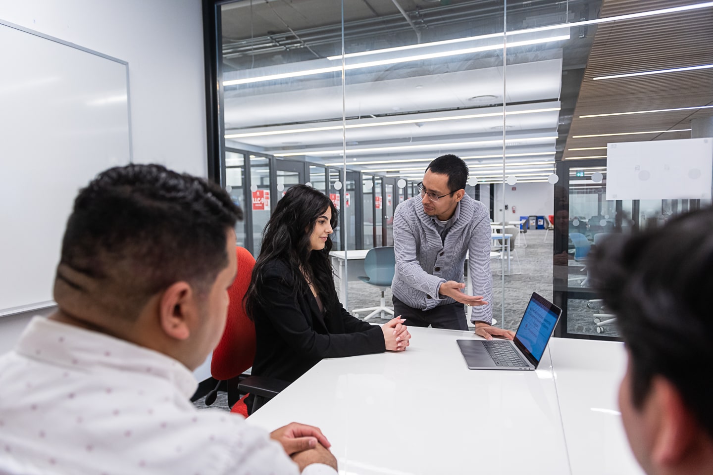 man gestures at laptop while others sit around boardroom table