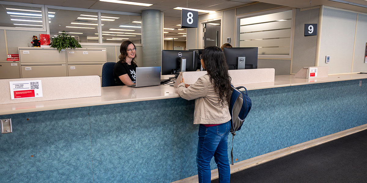 student stands at desk talking to Registrar staff