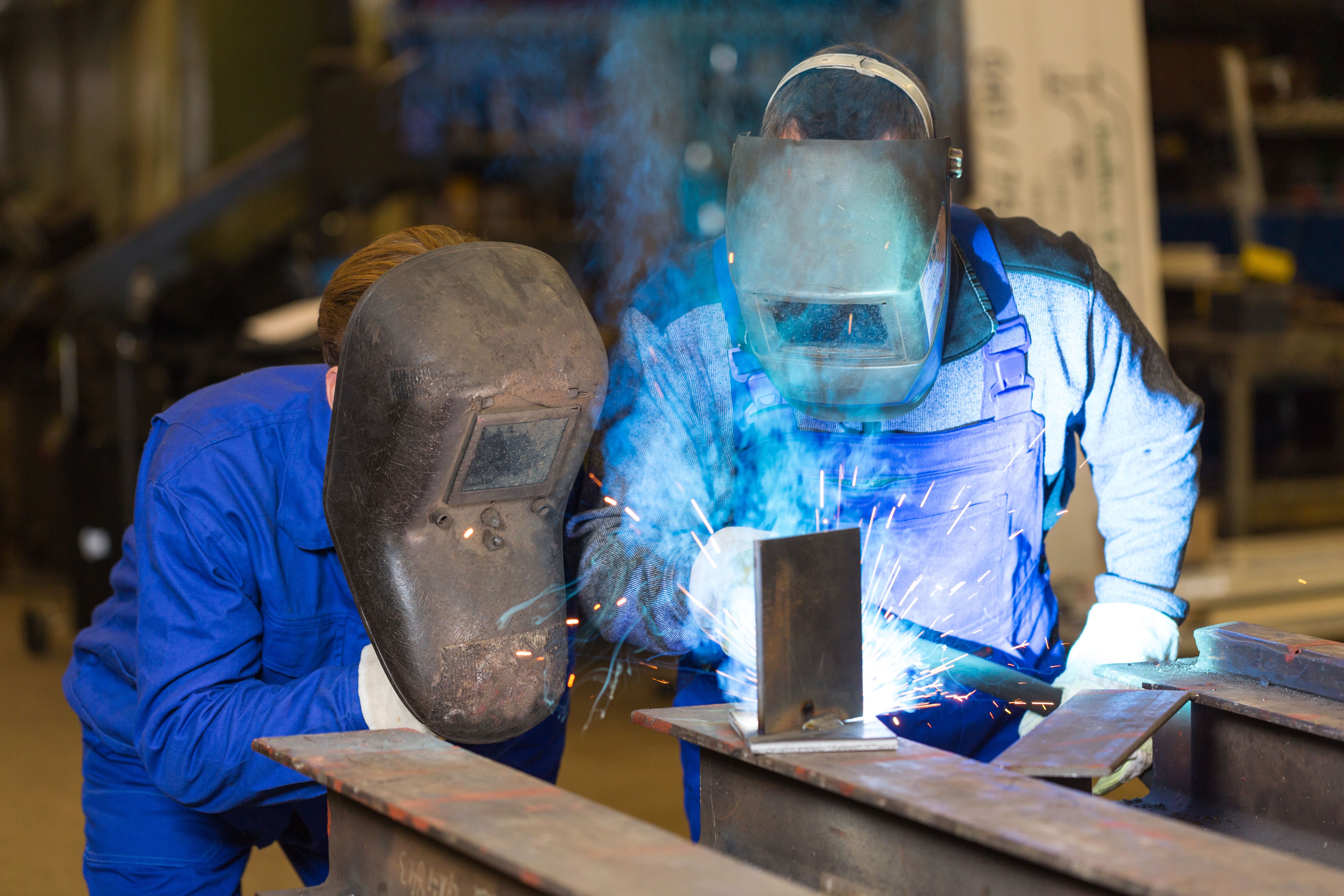 Two welders wearing masks work together