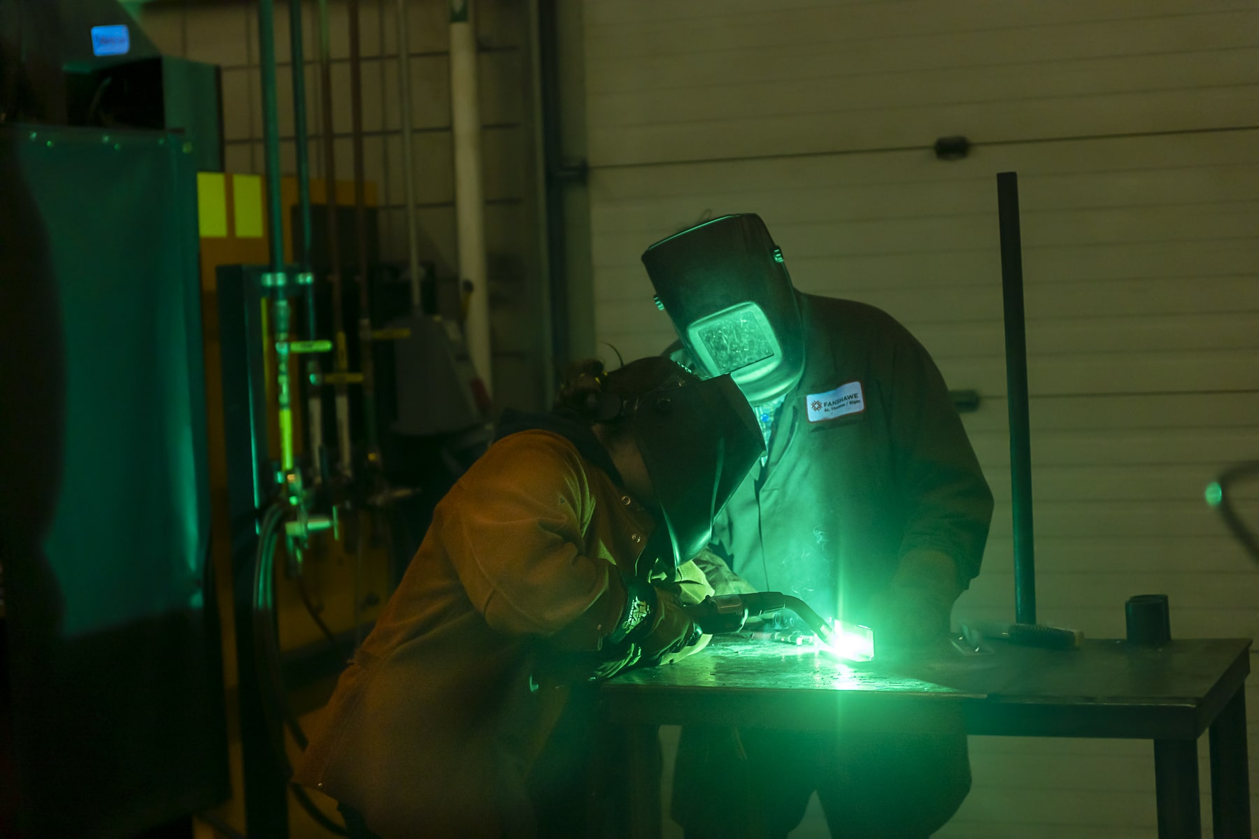 Mind Over Metal Camp welders lean over their work lit by green welding light