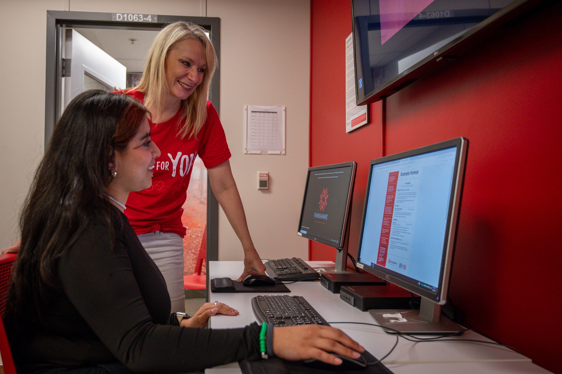 advisor stands next to student who is editing resume on computer