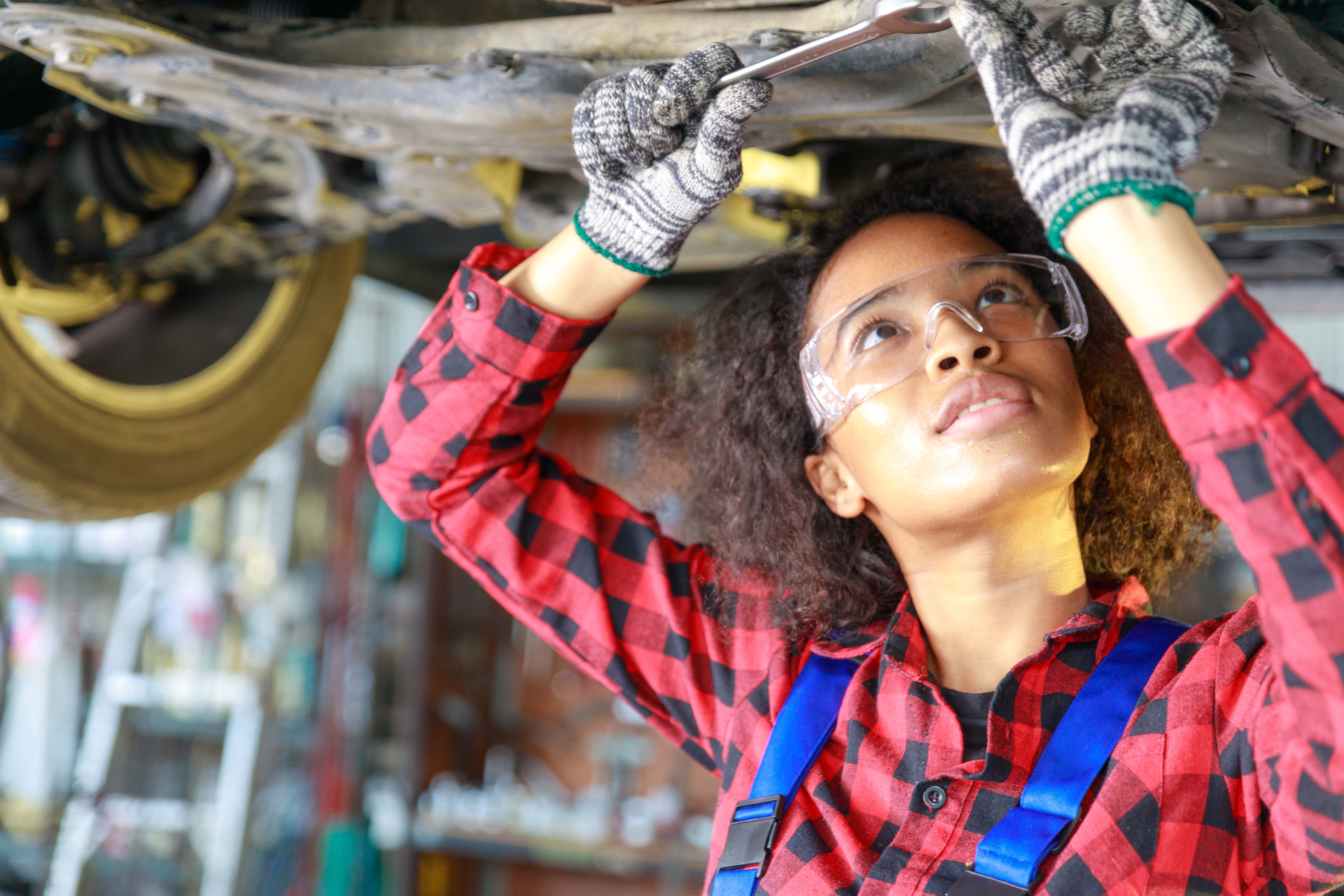woman wearing PPE works on underside of vehicle