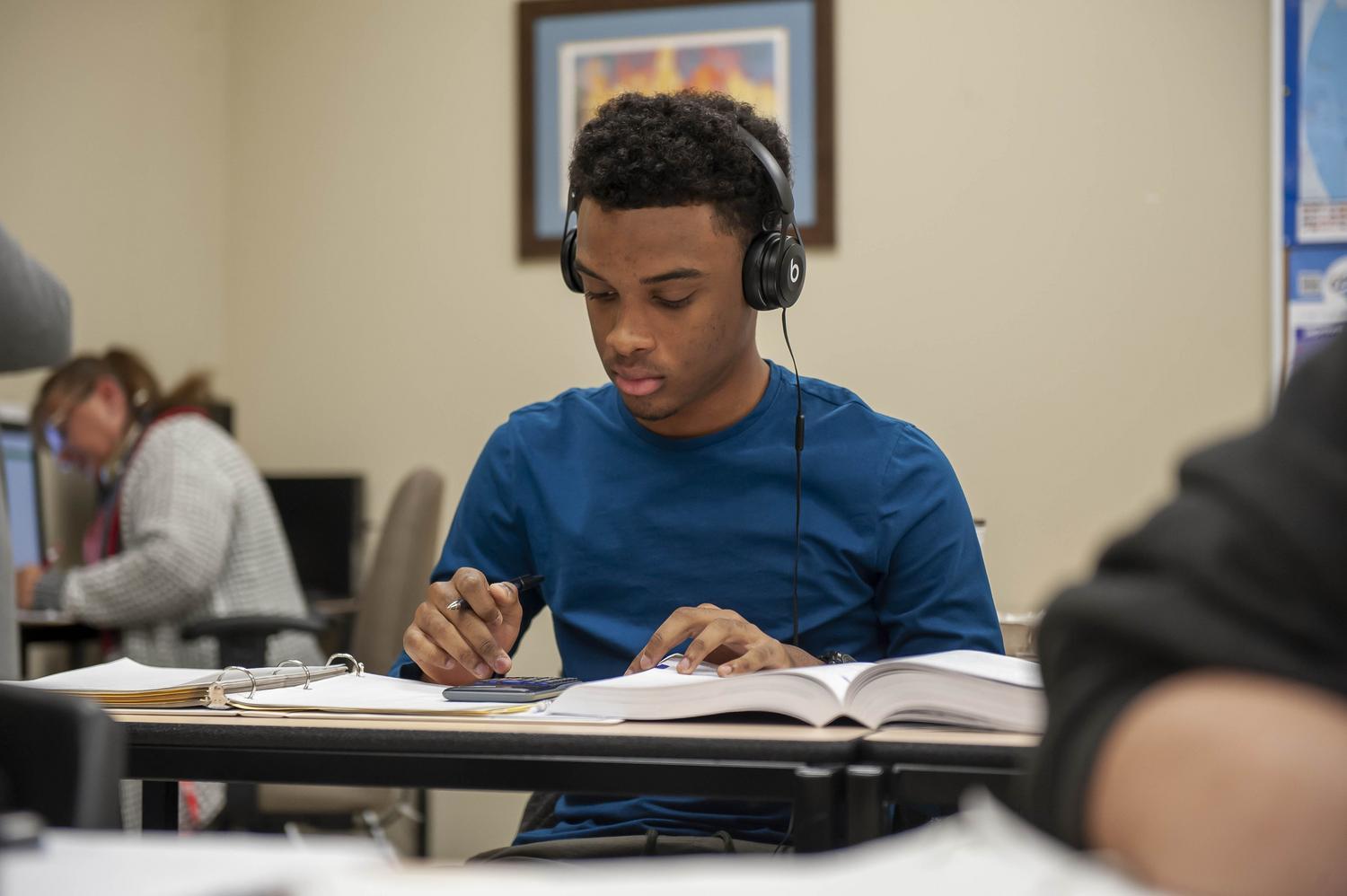 Student writing while wearing a headphone