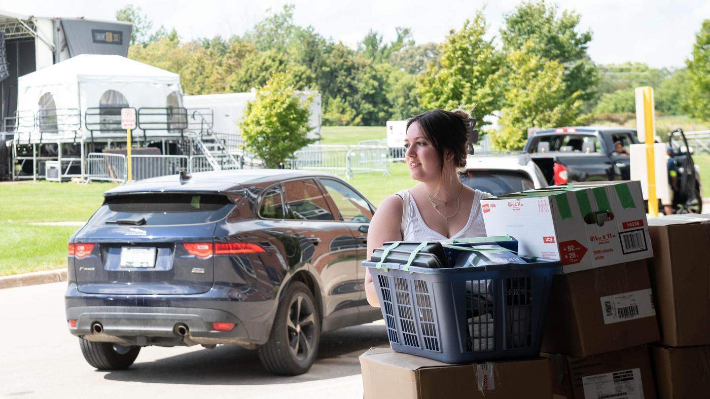 student stands by stack of packed boxes for moving