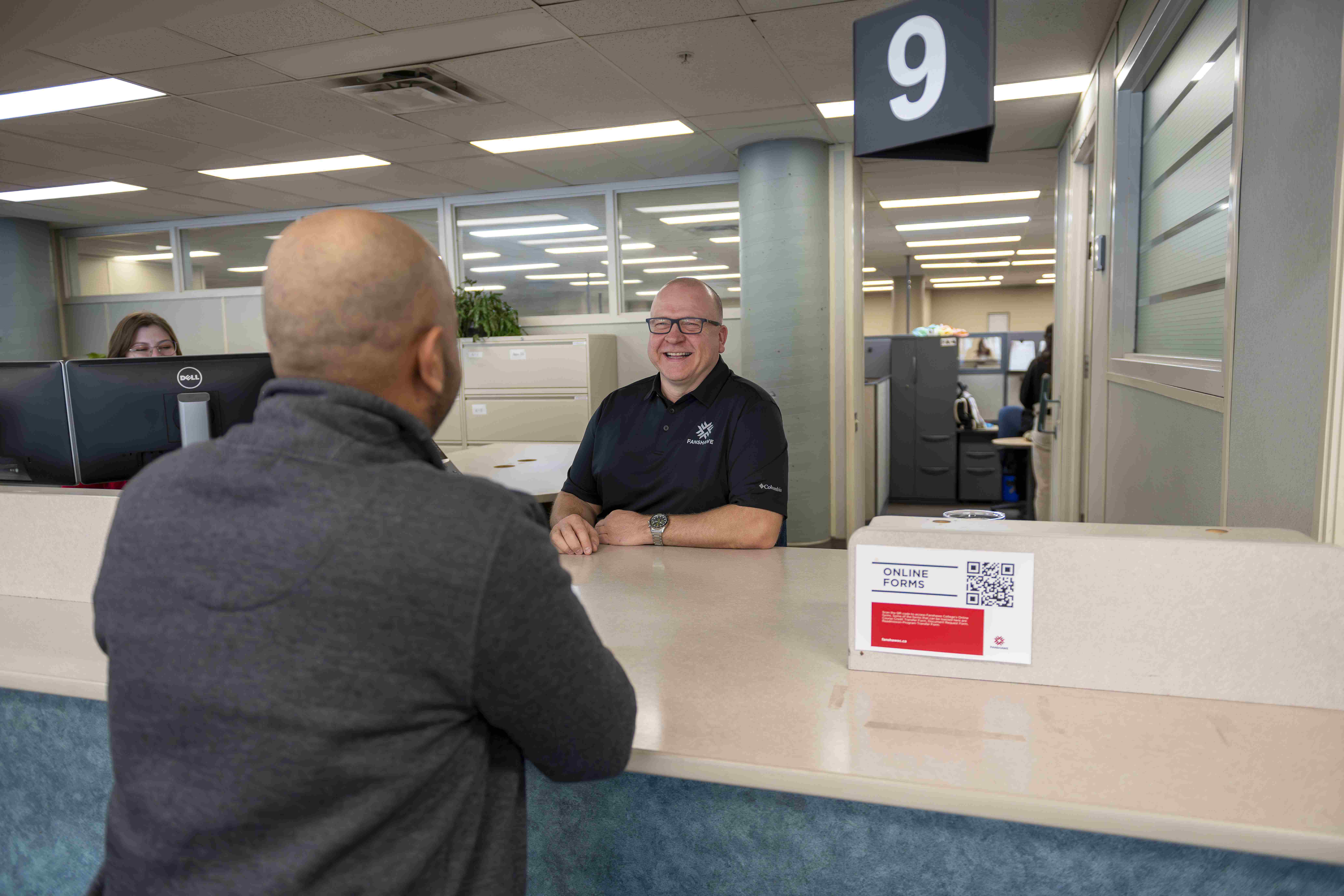 A Fanshawe employee behind a service desk helping a student who is asking questions