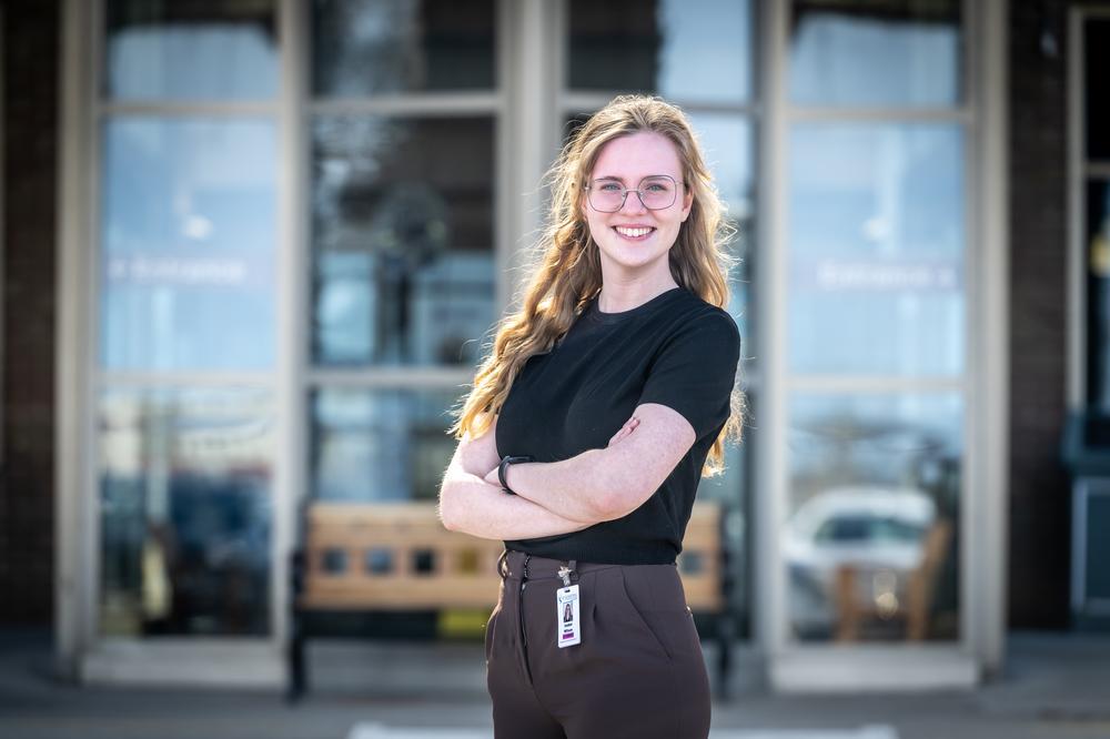 A Fanshawe grad posing in front of a building entrance with their hands crossed and smiling