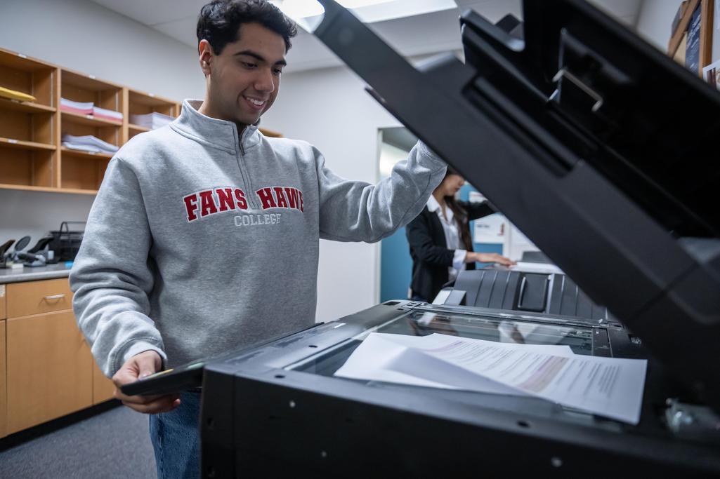 A Fanshawe student opening a printer and looking at the pages inside